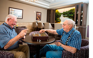 Two elderly gentleman smiling and laughing while playing chess