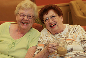 Two elderly women laughing and smiling at the camera