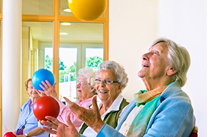 An group of elderly women laughing and smiling as they play with large bouncy-balls