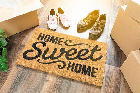 A welcome mat that says 'Home Sweet Home' with a couple of shoes and boxes surrounding it