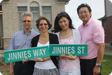 Two couples stand, holding two street signs, one that says Jinnies Way and one that says Jinnies St