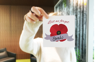 An individual holding up a sticker with a poppy and 'lest we forget'
