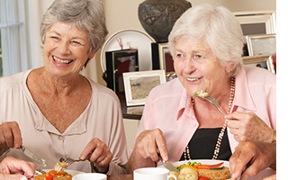 Two elderly women smiling while they share a meal